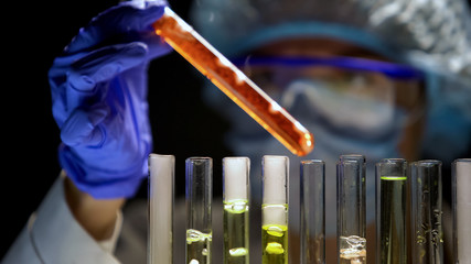 Lab assistant checking tube with orange liquid in darkness, special conditions
