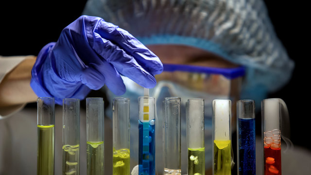 Scientist measuring acidity level in tube with blue liquid in dark laboratory
