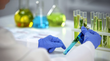 Biochemist looking at plant in tube with blue liquids, preservatives, reaction