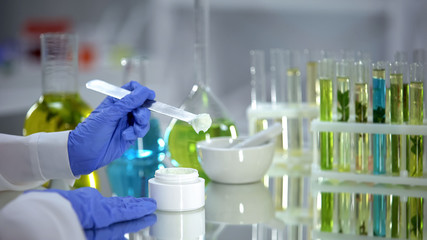 Biochemist taking creme sample from tube, organic beauty production, dermatology