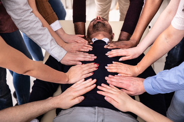 Group Of Hands Touching Man's Body Lying On Table