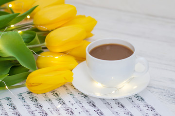 yellow tulips with garlands, a cup of coffee, cappuccino and notes on a white wooden background