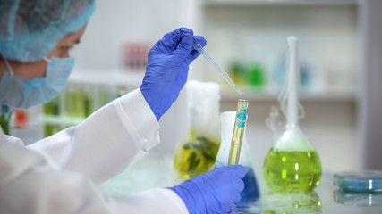 Scientist adding blue liquid in tube with yellow oily substance, biofuel testing