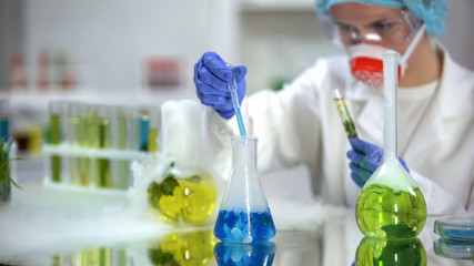 Lab researcher adding blue liquid substance in tube with green plant, test