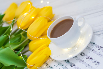 yellow tulips with garlands, a cup of coffee, cappuccino and notes on a white wooden background