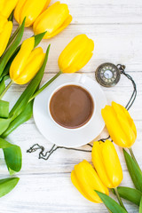 yellow tulips, a cup of coffee, cappuccino and vintage watch on a chain on a white wooden background