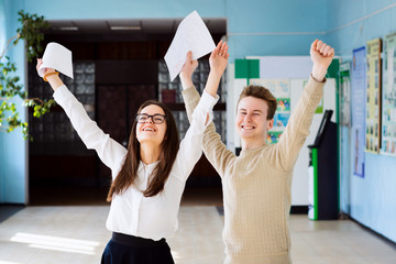 Two happy friends happy after researching their checked exams, raising hands up and expressing amusement of getting excellent grades for their work
