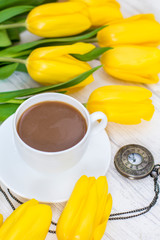 yellow tulips, a cup of coffee, cappuccino and vintage watch on a chain on a white wooden background
