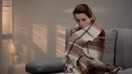 Lonely depressed female sitting on couch, covered with plaid, unemployment