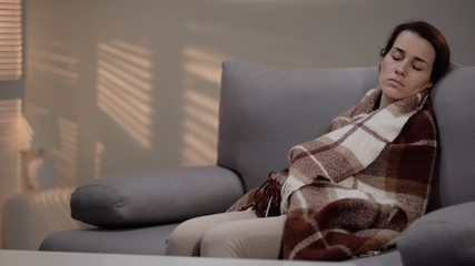 Obraz premium Lonely young depressed female sleeping on couch, covered with plaid, despair