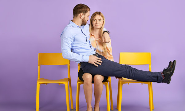Friendly male and female coworkers having fun and playing crazy. Young man sitting on woman's lap and looking at her and waiting for job interview - Powered by Adobe