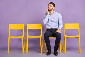 studio shot of young man in deep thoughts sitting on chair and waiting for job interview