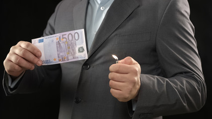 Man in suit burning five hundred euro bill, money wasting, bankruptcy concept