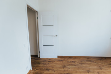 modern light interior. room with white walls and wooden floor. white open door.