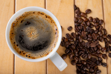 White cup with black coffee on a wooden table. A grain of coffee and a hot drink.
