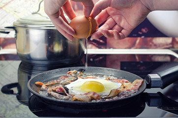 chef breaks egg into frying pan, cooks bacon and fried eggs in frying  pan, cooks in kitchen, close up front view