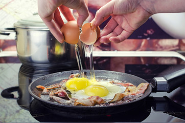 chef breaks egg into frying pan, cooks bacon and fried eggs in frying  pan, cooks in kitchen, close up front view