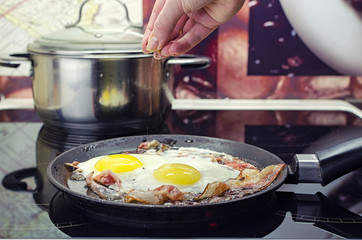 the chef salts the fried eggs in a frying pan, cook the bacon and fried eggs in the frying pan, cooking in the kitchen, puts the spices in the scrambled eggs, closeup front view