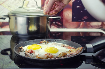 the chef salts the fried eggs in a frying pan, cook the bacon and fried eggs in the frying pan, cooking in the kitchen, puts the spices in the scrambled eggs, closeup front view