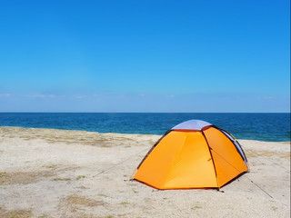 orange tent on the sand against the background of the sea and sky