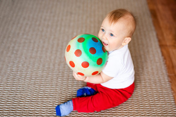 Fototapeta na wymiar Little baby boy in white t-shirt with a toys on the floor at home