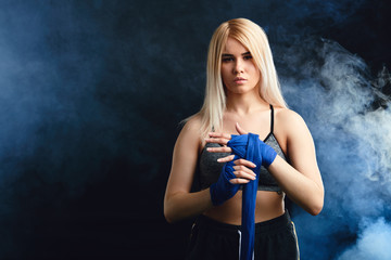 Handsome caucasian blonde woman fighter wrapping her hands with a band, preparing herself in boxing arena sport