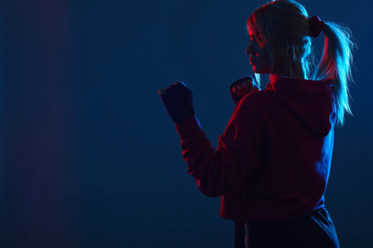Silhouette of Female Muay Thai fighter with hairs tied in ponytail, standing in defensive stance at the corner over dark blue background with copy space