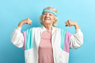 Happy, proud elderly attractive woman flexing both arms in the air with fists pressed showing...