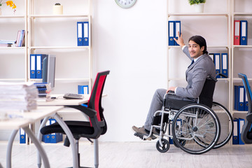 Young handsome employee in wheelchair working in the office  