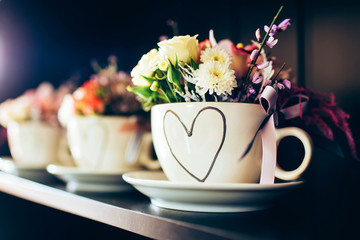 white cup with a heart on the shelf. bouquet of roses, carnations and asters.