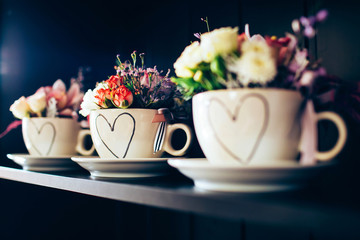 white cup with a heart on the shelf. bouquet of roses, carnations and asters.
