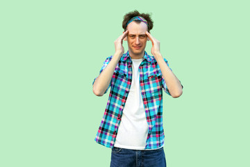 Headache or confuse. Portrait of sad or sick young man in casual blue checkered shirt and headband...