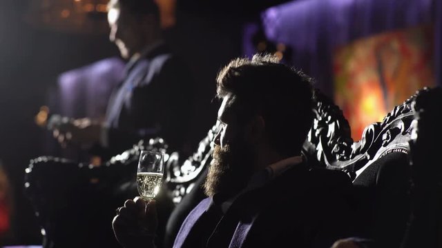 Bearded man with serious face and security man. Criminal boss in luxury suit sits on vintage sofa. Mature man with beard talks to his assistant. Crime, mafia, gangster concept. Luxury rich lifestyle.