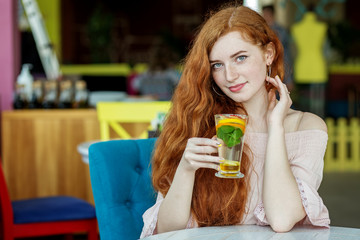 Red-haired girl smiles in a cafe. Tea with mint and citrus. Concept of lifestyle, drinks and healthy eating