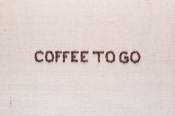 Coffee to go written with coffee beans on linen canvas, arranged in center