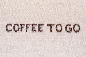 Coffee to go written with coffee beans on linen canvas, shot close up