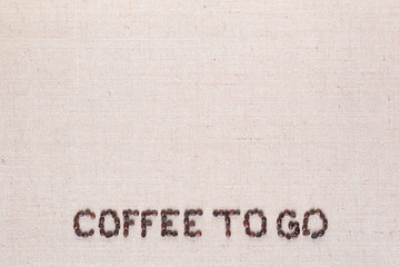 Coffee to go written with coffee beans on linen canvas, arranged bottom center