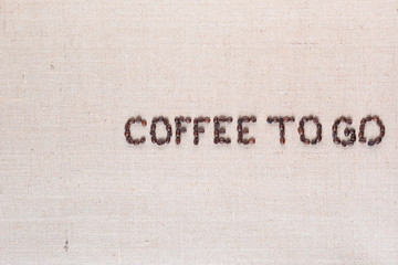 Coffee to go written with coffee beans on linen canvas, arranged middle right