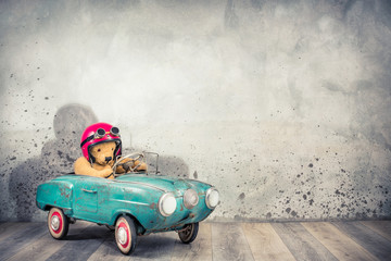 Retro Teddy Bear toy racer in old helmet hat with aviator goggles driving antique rusty turquoise...