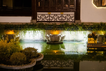 Illuminated stone flower sculpture floating in water pond near the ancient china culture building reflected in water