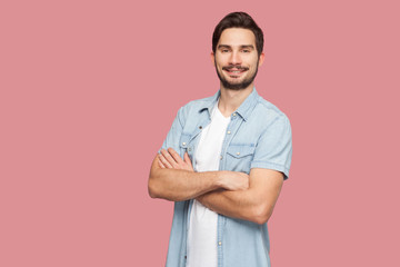 Fototapeta premium Portrait of happy successful handsome bearded young man in blue casual style shirt standing, raised arms and looking at camera with toothy smile. indoor studio shot, isolated on pink background.