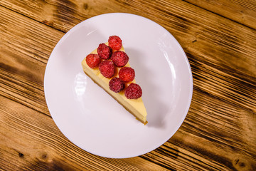 White plate with cheesecake New York and raspberries on wooden table. Top view