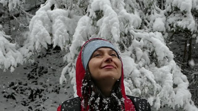 The girl rejoices in the snow in winter. Beautiful snowfall. Snow-covered trees in the forest.