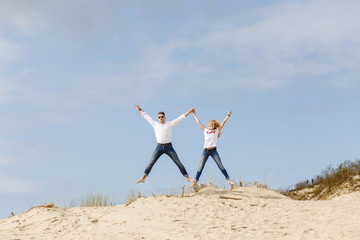 Obraz premium boy and girl jumping in the sand dunes in summer on a sunny day
