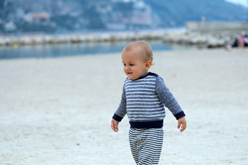 Fototapeta na wymiar Cute Baby Boy Wearing A Sweater On The Sandy Beach