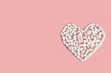 heart laid out of white and pink mini marshmallows on a pink background