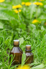 pharmaceutical bottle of medicine in grass against background of blooming yellow flower Taraxacum officinale, or dandelions . Preparation of medicinal plants. Ready potion of grass.
