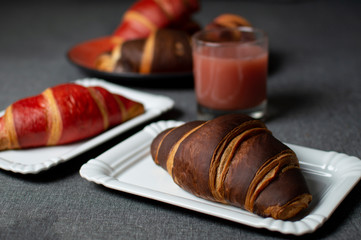chocolate and red croissants lie with a glass of juice on plates on a gray cloth, close-up of a bun