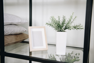 Modern potted evergreen artificial plant used in interior decoration. Plant on a shelf next to a photo frame