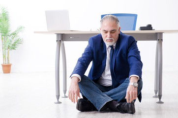 Aged businessman doing yoga exercises in the office 